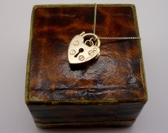 May include: A gold heart-shaped padlock pendant on a gold chain. The pendant is in a brown leather box.
