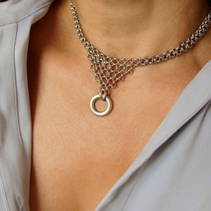 May include: A silver chain necklace with a large, round pendant. The necklace is made of multiple strands of chain, and the pendant is a simple circle.