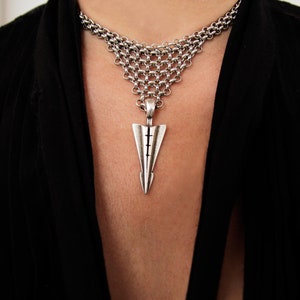 May include: A silver chain necklace with a silver arrow pendant. The necklace is layered and features a delicate chain design.