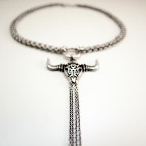 May include: A silver chain necklace with a bull skull pendant and a long, dangling chain with multiple strands.