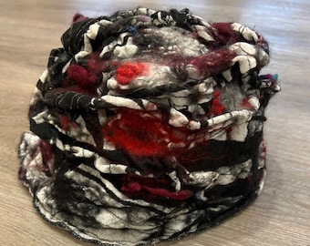 May include: A black, white, red and burgundy felted wool hat with a unique, abstract design. The hat is made of layers of fabric that have been felted together to create a textured, three-dimensional effect.