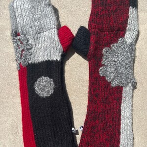 May include: A pair of fingerless gloves with a patchwork design. One glove is red, black, and gray, while the other is gray and red. The gloves are knitted with a textured pattern.