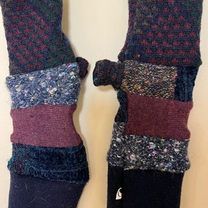 May include: A pair of fingerless gloves made from a patchwork of different fabrics. The gloves are black, burgundy, green, and blue with a variety of textures. The gloves have a thumb hole and a fold-over cuff.