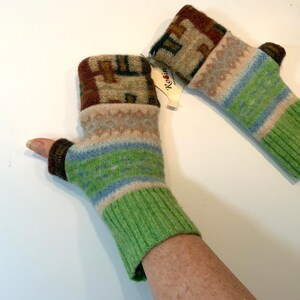 May include: A pair of green, blue, and brown fingerless gloves with a white and brown patterned cuff. The gloves are made of recycled wool and have a tag that says "Re:in".