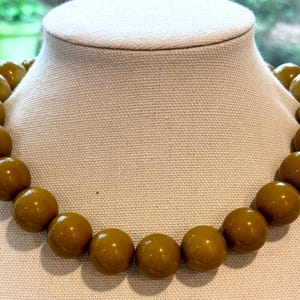 Puede incluir: Un collar hecho de grandes cuentas redondas, brillantes y de color verde oliva.