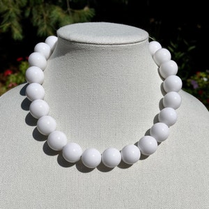May include: A white beaded necklace with large, round beads. The necklace is displayed on a mannequin, showcasing its circular shape and bright white color. The beads appear to be evenly sized and spaced.