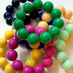 May include: A close-up of a collection of colorful plastic beads in various shades of green, pink, yellow, blue, and white. The beads are arranged in a circular pattern, creating a visually appealing and vibrant display.