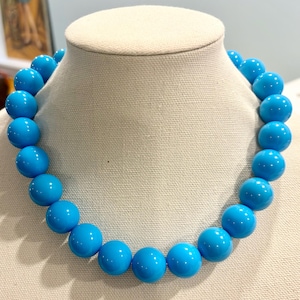 May include: A turquoise blue beaded necklace with large, round beads. The necklace is displayed on a white mannequin.