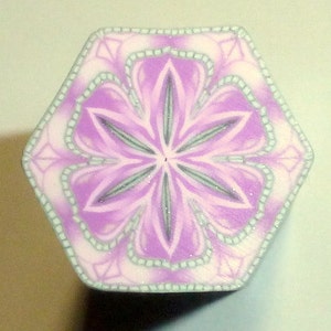 May include: A hexagonal purple and white polymer clay tile with a detailed floral design. The center of the tile features a six-pointed star with a white center.