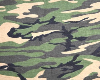May include: Camouflage fabric with a pattern of green, brown, and black shapes. The fabric has a soft, textured feel.