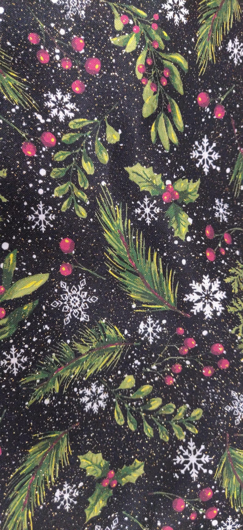 May include: A black fabric featuring a festive holiday pattern of green pine branches, holly leaves, red berries, and white snowflakes. The design includes subtle gold glitter accents scattered throughout the dark background, creating a shimmering effect.