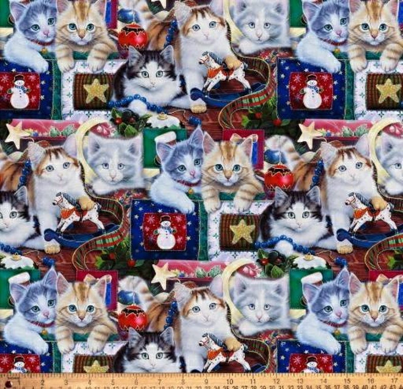 May include: A colourful fabric featuring a repeating pattern of kittens in various poses, surrounded by Christmas-themed decorations such as ornaments, presents, and a rocking horse. The fabric is a blend of red, green, blue, and white.