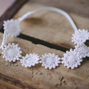 May include: White lace headband with a delicate floral design. The headband is made of a soft, flexible material and is perfect for adding a touch of elegance to any outfit.