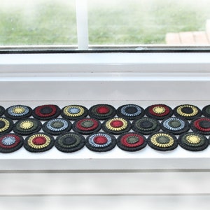 May include: A row of colorful crocheted circles in shades of green, red, yellow, and blue. The circles are arranged in a pattern and are made of yarn.