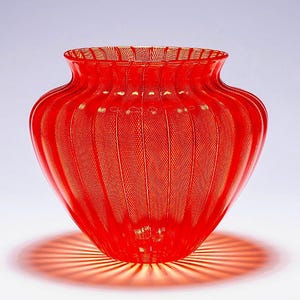 May include: A vibrant red glass vase featuring a distinct ribbed, vertical texture throughout its rounded body. The translucent material allows light to pass through, creating a radiating shadow pattern on the surface beneath the base.