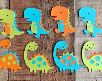 May include: A set of eight paper dinosaur cutouts in two distinct shapes. The top row features four bipedal dinosaurs in lime green, blue, and orange. The bottom row displays four long-necked sauropod dinosaurs in orange, lime green, and blue.