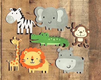 May include: A collection of seven paper cutouts featuring cartoon animals including a black and white zebra, a gray elephant, a brown monkey, a green crocodile, a yellow giraffe with orange spots, a lion with an orange mane, and a gray hippo.