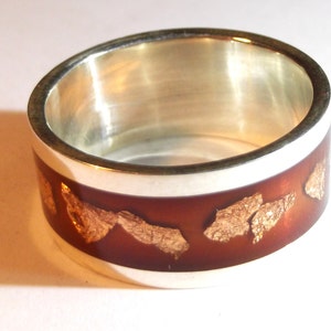 May include: A silver ring with a red band and gold flakes embedded in the red band.