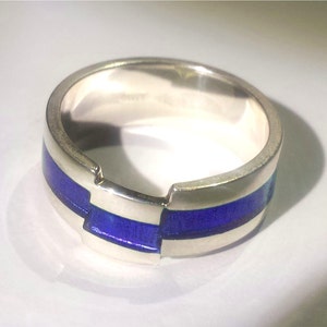 Op de afbeelding: Een zilveren ring met een blauwe emaille inlay. De ring heeft een uniek ontwerp met een breuk in de band.