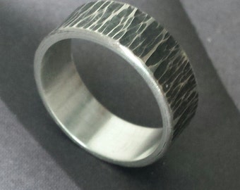 May include: A silver ring with a textured, hammered finish. The ring is wide and has a smooth inner band.