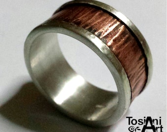 May include: A silver and copper band ring with a textured copper surface. The ring is wide and has a polished silver edge.