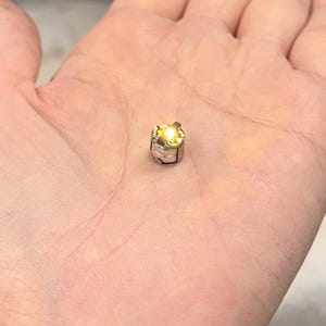 May include: A small, metallic, cylindrical object with a bright yellow light emanating from the top. The object is held in the palm of a hand, and the light is the focal point of the image.