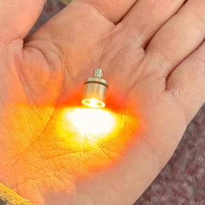 May include: A small, silver-colored light bulb with a warm, orange glow.