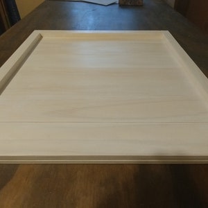 May include: White wooden tray with a raised edge. The tray is made of several pieces of wood that have been joined together. The tray is sitting on a wooden surface.
