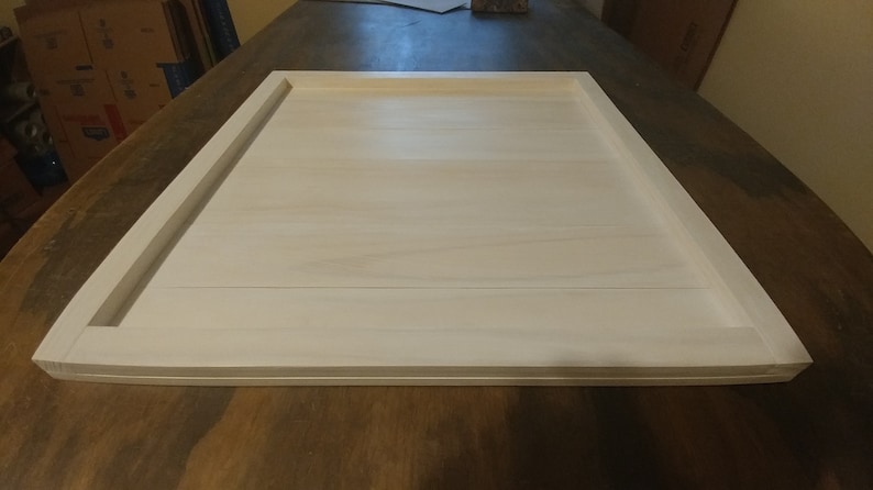 May include: White wooden tray with a raised edge. The tray is made of several pieces of wood that have been joined together. The tray is sitting on a wooden surface.