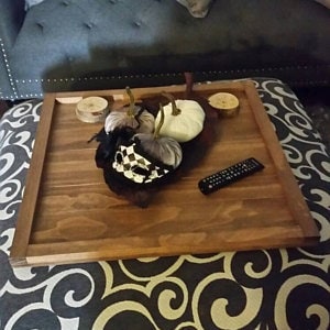 May include: A large, rectangular wooden tray with a dark brown stain. The tray has a raised edge and is sitting on a patterned fabric surface. There are two white pumpkins and a decorative object on the tray.