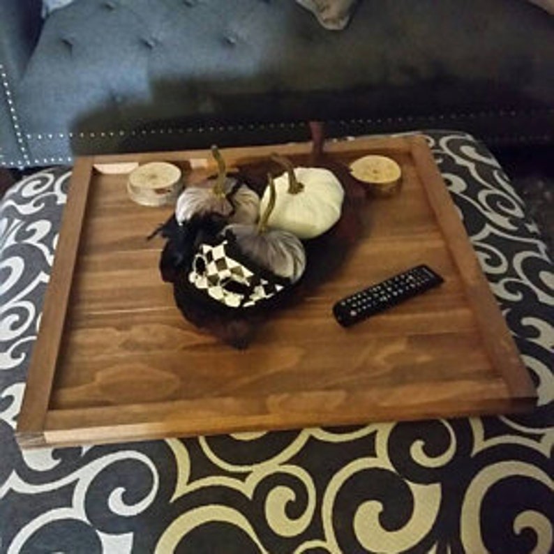 May include: A large, rectangular wooden tray with a dark brown stain. The tray has a raised edge and is sitting on a patterned fabric surface. There are two white pumpkins and a decorative object on the tray.