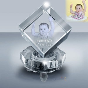 May include: A clear crystal cube with a 3D image of a baby girl inside. The cube is on a clear crystal base with a hexagonal shape. The text "Annabelle 7 lbs 3 oz" is engraved on the cube.