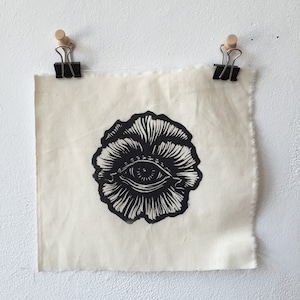 Könnte beinhalten: Schwarz-Weiß-Druck eines Auges in einer Blume auf weißem Stoffhintergrund.