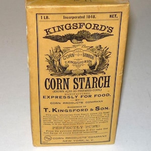 May include: A rectangular yellow box of Kingsford's Corn Starch with black text and graphics. The label features an eagle, two figures, and the text 1 LB. NET. The packaging includes historical branding details and product information printed on the front.