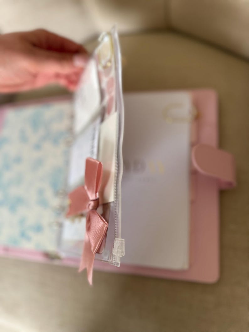 A hand holding a pink binder with a clear zipper, and a white paper inside the binder.