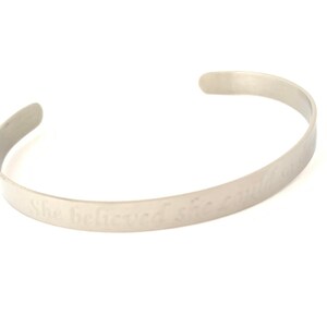 May include: A silver bangle bracelet with the inscription "She Believes She Will So She Does".