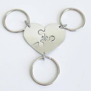 May include: Three silver keychains with interlocking puzzle pieces in the shape of a heart. Each keychain has a separate ring.