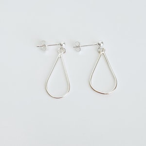 May include: A pair of silver teardrop earrings. Each earring features a post with a small ball and a delicate, open teardrop shape. The earrings are displayed against a plain white background, highlighting their simple elegance.