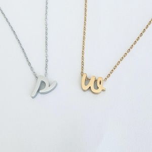 May include: Two delicate necklaces with cursive letter pendants. One necklace is silver with a letter "P" pendant, and the other is gold with a "W" pendant. Both necklaces have thin chains.