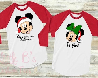 May include: Two red and white baseball shirts with a Christmas theme. One shirt features Mickey Mouse wearing a Santa hat with the text "All I want for Christmas..." The other shirt features Minnie Mouse wearing a Santa hat with a green bow and the text "Is You!"