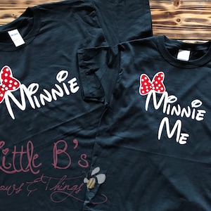 Puede incluir: Dos camisetas negras con texto blanco y un lazo rojo con lunares blancos. La camiseta m&aacute;s grande dice "Minnie" y la m&aacute;s peque&ntilde;a dice "Minnie Me".