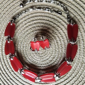 May include: A jewelry set consisting of a necklace and matching clip-on earrings. The necklace features a silver-toned metal chain with alternating red, tooth-shaped resin links. The earrings are shaped like single red teeth with silver-toned metal clips.
