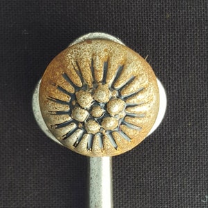 May include: A silver hook with a round, decorative top. The top is gold with a black and silver design.