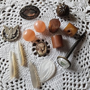 May include: Assortment of vintage buttons and other decorative items, including a silver-toned eagle pin, a carved wooden knob, and several mother-of-pearl buttons.