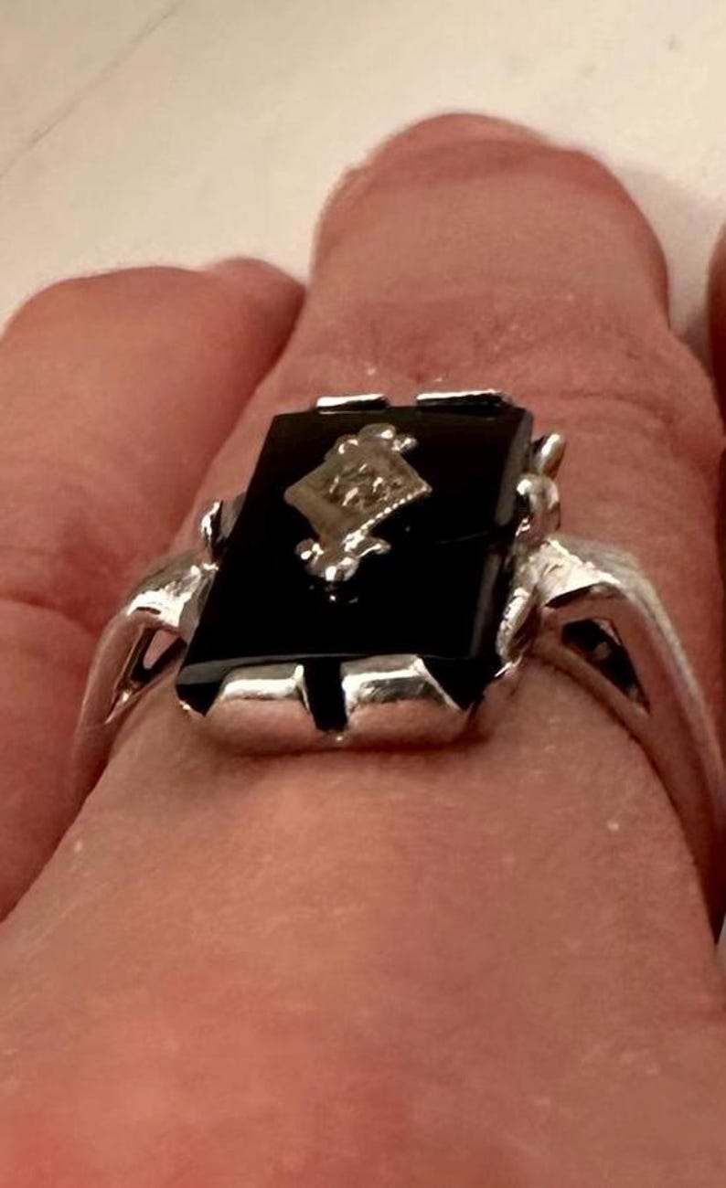 May include: A silver ring with a rectangular black onyx stone. The ring features a diamond-shaped design in the center of the onyx and a silver band. The ring is a classic piece of jewelry.