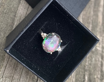 May include: A ring with a large oval-shaped iridescent gemstone surrounded by smaller clear gemstones. The ring is in a black velvet ring box.