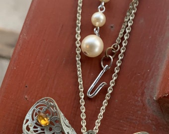 May include: A silver chain necklace with a delicate butterfly pendant. The butterfly is made of filigree metal and has colorful rhinestones. The necklace also has a strand of pearls.