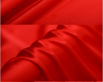May include: A close-up of a bright red satin fabric. The fabric is smooth and silky, with a slight sheen. The fabric is folded in several places, showing the drape and texture.