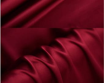 May include: Close-up of a deep red satin fabric with a smooth, silky texture. The fabric is folded and draped, showcasing its luxurious drape and sheen.