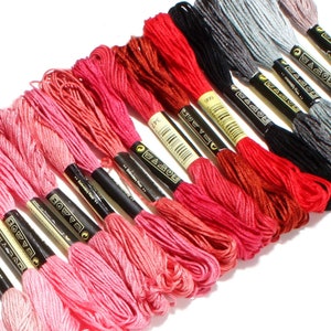 May include: A collection of embroidery floss spools in various shades of pink, red, and grey. The spools are arranged in a row, with the pink shades at the bottom and the grey shades at the top. The spools are labeled with the brand name "DMC" and the color number.